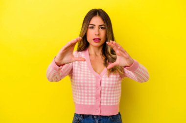 Sarı arka planda izole edilmiş genç beyaz kadın elinde avuç içi bir şeyle kameraya sunuyor..