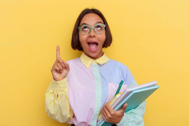 Sarı arka planda izole edilmiş, ağzı açık, üst tarafı işaret eden genç ırk öğrencisi kadın..