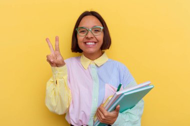 Sarı arka planda izole edilmiş genç bir ırk öğrencisi. İki numarayı parmaklarıyla gösteriyor..