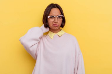 Genç öğrenci melez kadın sarı arka planda izole edilmiş kafasının arkasına dokunuyor, düşünüyor ve bir seçim yapıyor..