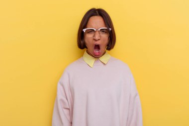 Genç öğrenci melez kadın sarı arka planda izole edilmiş çok kızgın ve agresif bağırıyor..