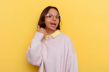 Sarı arka planda izole edilmiş genç öğrenci ırk kadını parmaklarıyla bir cep telefonu hareketi gösteriyor..