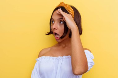 Genç melez kadın, sarı arka planda izole edilmiş. Uzağa bakıyor, elini alnına koyuyor..