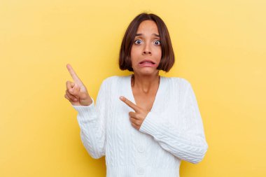 Sarı arka planda izole edilmiş genç melez kadın işaret parmağıyla fotokopi alanını işaret ederek şok oldu..