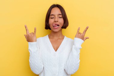 Sarı arka planda izole edilmiş genç melez kadın parmaklarıyla kaya hareketi gösteriyor.