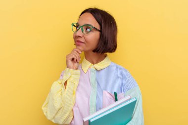 Sarı arka planda izole edilmiş genç melez kız şüpheli ve şüpheci bir ifadeyle yana bakıyor..