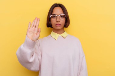 Sarı arka planda izole edilmiş, elini uzatmış, dur işareti gösteren genç bir ırk öğrencisi..