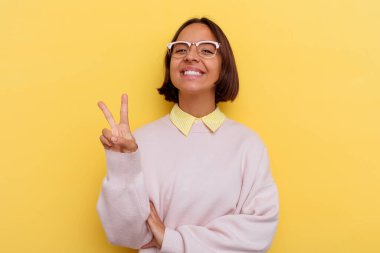 Genç öğrenci melez kadın sarı arka planda izole edilmiş iki numarayı parmaklarıyla gösteriyor..