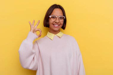 Genç öğrenci melez kadın, sarı arka planda izole edilmiş neşeli ve kendinden emin, iyi bir hareket gösteriyor..