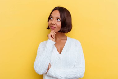 Sarı arka planda izole edilmiş genç melez kadın şüpheli ve şüpheci bir ifadeyle yana bakıyor..