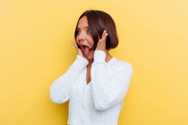 Sarı arka planda soyutlanmış genç melez kadın yüksek sesle bağırıyor, gözleri açık ve elleri gergin tutuyor..