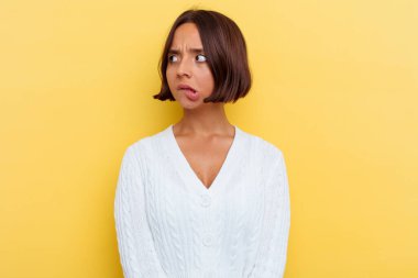 Sarı arka planda izole edilmiş genç melez kadın kafası karışmış, şüpheli ve güvensiz hissediyor..