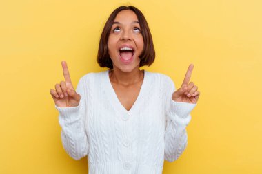 Sarı arka planda izole edilmiş, ağzı açık, üst tarafı gösteren genç melez bir kadın..