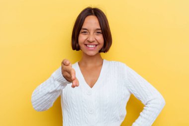 Sarı arka planda izole edilmiş genç bir ırk kadını selamlama jesti olarak kameraya elini uzatıyor..