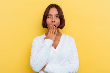 Sarı arka planda soyutlanmış genç melez bir kadın esniyor. Ağzı eliyle kapatan yorgun bir jest yapıyor..