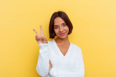 Sarı arka planda izole edilmiş genç melez kadın neşeli ve tasasız parmakları olan bir barış sembolü gösteriyor..