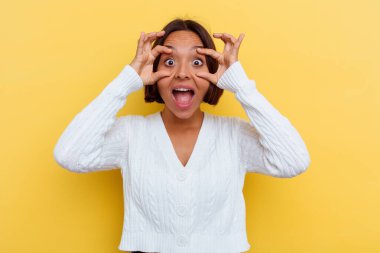 Sarı arka planda izole edilmiş genç melez kadın bir başarı fırsatı bulmak için gözlerini açık tutuyor..