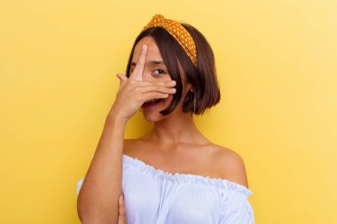 Sarı arka planda izole edilmiş genç bir ırk kadını parmaklarıyla kameraya göz kırpıyor ve yüzünü kapatmaktan utanıyor..