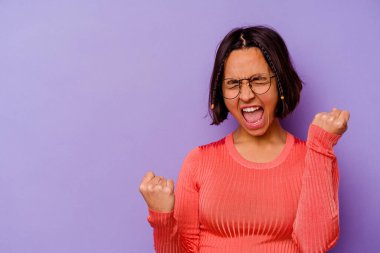 Mor arka planda izole edilmiş genç bir ırk kadını zafer sonrası yumruğunu kaldırıyor, kazanan konsept..