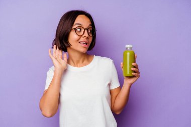Mor arka planda izole edilmiş sağlıklı bir smoothie tutan genç bir ırk kadını bir dedikoduyu dinlemeye çalışıyor..