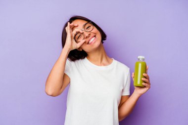 Mor arka planda izole edilmiş sağlıklı bir smoothie tutan genç bir ırk kadını heyecanlı..