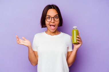 Mor arka planda izole edilmiş sağlıklı bir smoothie 'yi tutan genç melez kadın şaşırmış ve şok olmuş..