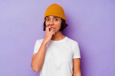 Mor arka planda yünlü şapka takan, tırnak yiyen, gergin ve endişeli genç bir ırk kadını..