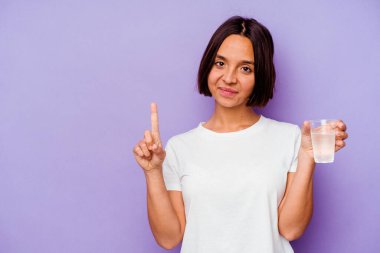 Mor zemin üzerinde bir bardak su tutan genç melez ırk parmak ile bir numarayı gösteriyor..