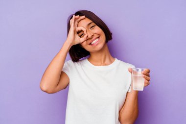 Mor arka planda izole edilmiş bir bardak su tutan genç melez..