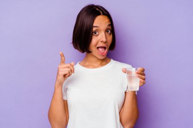 Mor arka planda izole edilmiş bir bardak su tutan genç melez ırkın bir fikri, ilham verici bir konsepti var..