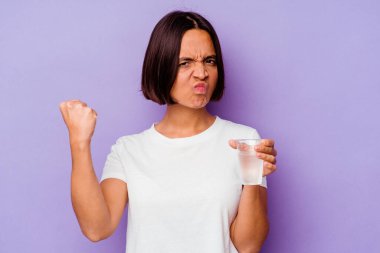 Mor arka planda izole edilmiş bir bardak su tutan genç bir ırk. Kameraya yumruk, agresif yüz ifadesi gösteriyor..