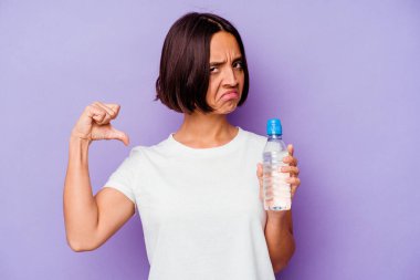 Mor arka planda izole edilmiş su şişesini tutan genç melez ırk gururlu ve kendinden emin hissediyor, örnek olarak..