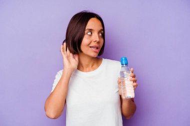 Mor arka planda izole edilmiş su şişesi tutan genç melez bir ırk bir dedikoduyu dinlemeye çalışıyor..