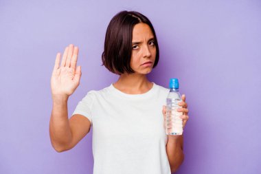 Mor arka planda izole edilmiş su şişesi tutan genç melez bir ırk. Kollarını uzatıp dur işareti göstererek seni engelliyor..