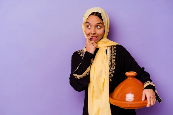 紫の背景に隔離されたタジンを持つ若いモロッコ人女性コピースペースを見て何かについてリラックスした考え — ストック写真