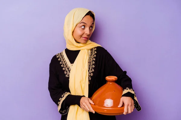 紫の背景に隔離されたタジンを持っている若いモロッコの女性は笑顔 陽気で楽しい脇に見えます — ストック写真