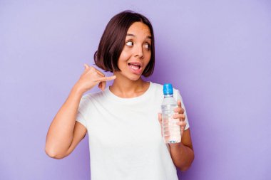 Mor arka planda izole edilmiş su şişesi tutan genç melez ırk parmakları olan bir cep telefonu hareketi gösteriyor..