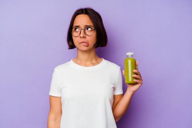 Mor arka planda izole edilmiş sağlıklı bir smoothie tutan genç melez kadın kafası karışmış ve kendinden emin değil..
