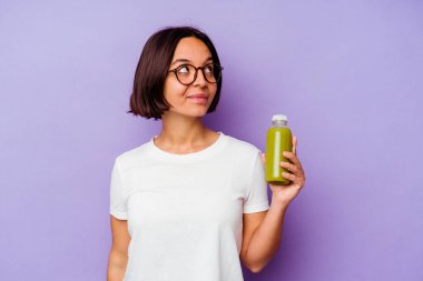 Mor arka planda izole edilmiş, amaçlarına ve amaçlarına ulaşmayı hayal eden sağlıklı bir smoothie 'yi tutan genç melez kadın.