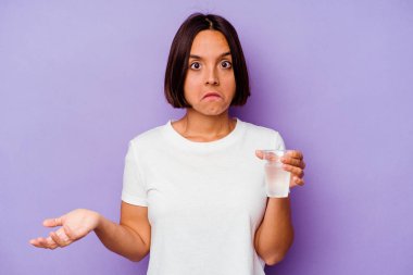 Mor arka planda izole edilmiş bir bardak su tutan genç melez ırk omuzlarını silker ve gözleri açık kalır..