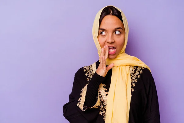 紫の背景に隔離された典型的なアラビアの衣装を身に着けている若いアラブ人女性は秘密のホットブレーキニュースを言っていると脇を見て — ストック写真