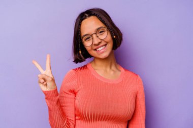 Mor arka planda izole edilmiş genç melez kadın neşeli ve tasasız parmakları olan bir barış sembolü gösteriyor..