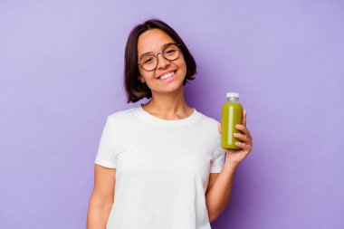 Mor arka planda izole edilmiş sağlıklı bir smoothie tutan genç melez kadın mutlu, güler yüzlü ve neşeli..