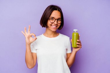 Mor arka planda izole edilmiş sağlıklı bir smoothie tutan genç bir ırk kadını neşeli ve kendinden emin bir şekilde iyi niyet gösteriyor..