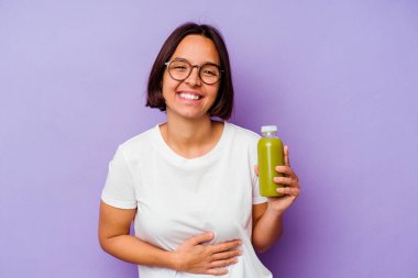 Mor arka planda izole edilmiş sağlıklı bir smoothie tutan genç bir ırk kadını gülüyor ve eğleniyor..