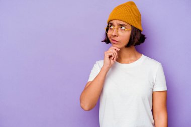 Mor arka planda yünlü şapka takan genç bir ırk kadını şüpheli ve şüpheci bir ifadeyle yana bakıyor..