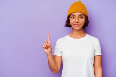 Mor arka planda izole edilmiş yün şapkalı genç bir ırk kadını parmak izleriyle bir numarayı gösteriyor..
