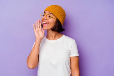 Mor arka planda izole edilmiş yün şapkalı genç bir ırk kadını bağırıyor ve avuç içini açık tutuyor..