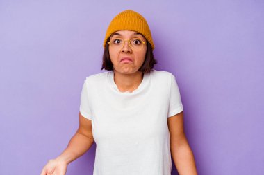 Mor arka planda izole edilmiş yün şapkalı genç bir ırk kadını omuzlarını silker ve gözleri açık kalır..