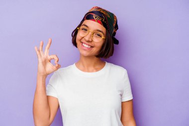 Mor arka planda izole edilmiş bandana takan genç bir ırk kadını neşeli ve kendinden emin bir şekilde iyi niyet gösteriyor..